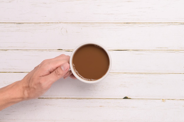 Mano che tiene una tazza da caffè su uno sfondo di legno