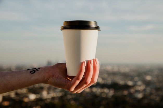 Mano che tiene una tazza di caffè da asporto con mockup di vista urbana