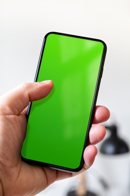 Mano che tiene uno smartphone con schermo verde vuoto Sfondo dell'ufficio