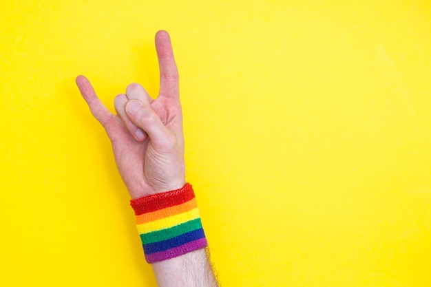 Mano con braccialetto bandiera arcobaleno gay pride su sfondo giallo