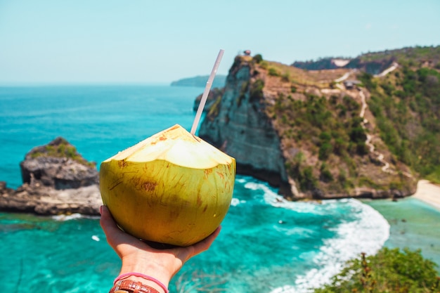 Mano con cocco sullo sfondo dell'oceano e delle scogliere