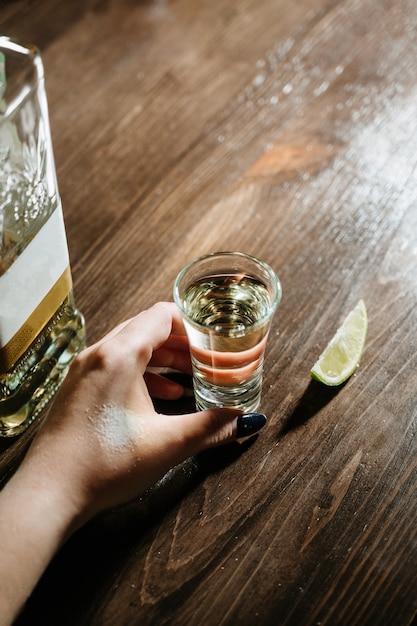 Mano con colpi di tequila sul tavolo di legno