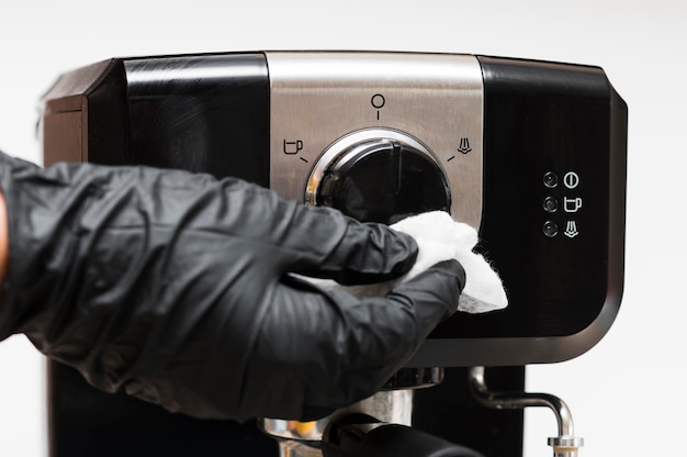 Mano con guanti che disinfettano la macchina per caffè istantaneo