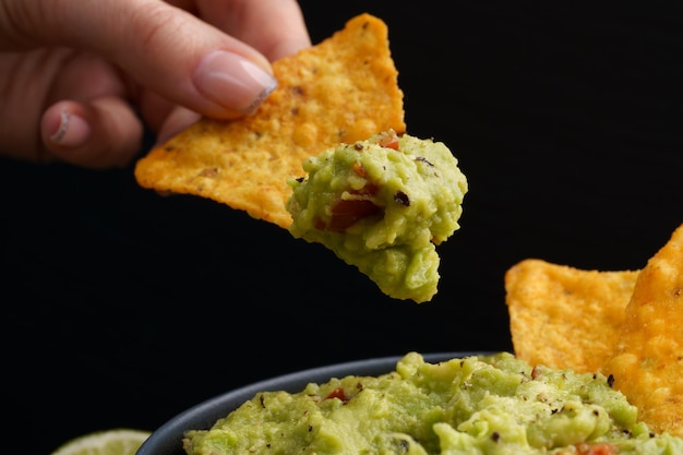 Mano con gustose tortilla chips o nachos con salsa di guacamole su sfondo nero