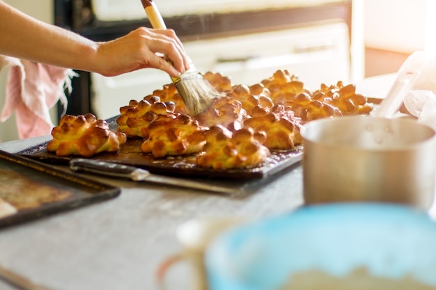 Mano con la pasta che tocca la spazzola. Pasta al forno su teglia da forno. La signora cuoce il cibo gustoso. Il lavoro inizia presto.