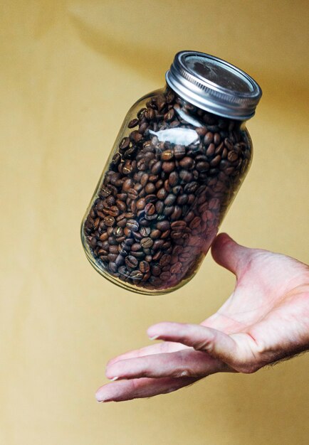 Mano con pentola di vetro piena di chicchi di caffè