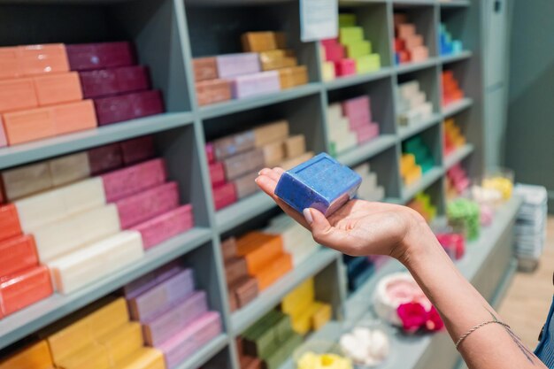 Mano con sapone a base di erbe di lavanda sullo sfondo di scaffali con una gamma di prodotti per la cura del corpo e cosmetici per il bagno