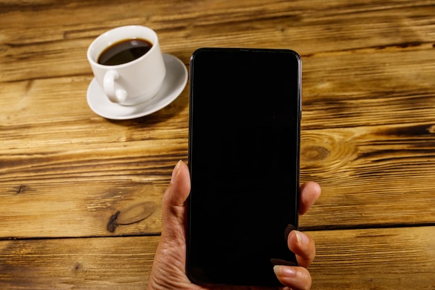 Mano con smartphone moderno e tazza di caffè su un tavolo di legno rustico