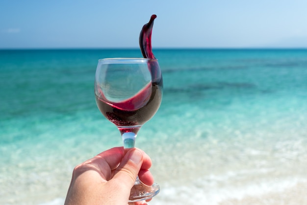 mano con un bicchiere di vino rosso sulla spiaggia durante la giornata di sole estivo