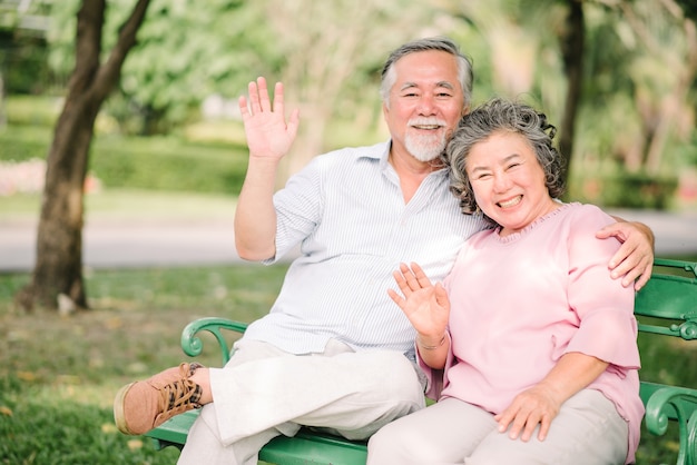 Mano d&#39;ondeggiamento delle coppie senior asiatiche felici e sorridere all&#39;aperto nel parco