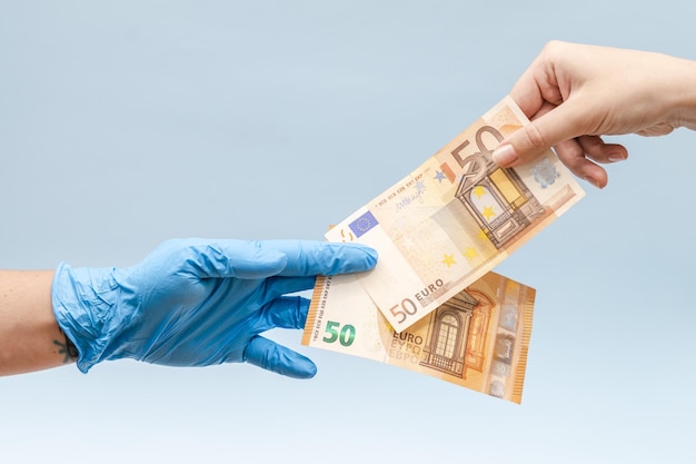 Mano d'uomo che dà soldi in euro a una mano in guanti chirurgici blu infermiere o medico Corruzione in medicina