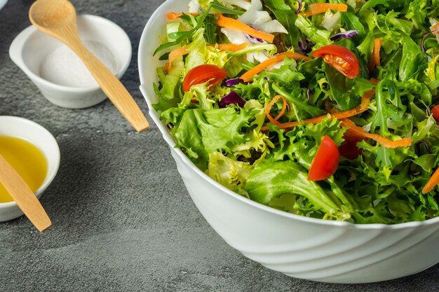 Mano d'uomo che serve insalata di lattuga, pomodori, rucola, varie verdure verdi con pinze di legno