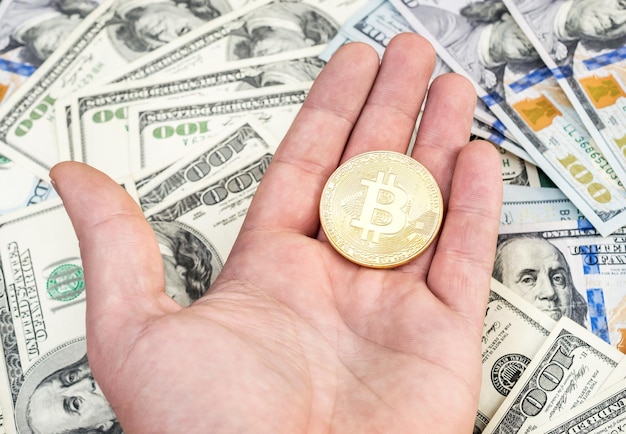 Mano d'uomo che tiene bitcoin dorato su sfondo di dollari USA