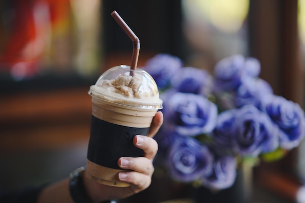 Mano d'uomo che tiene un bicchiere di frullato con sfondo floreale in un caffè