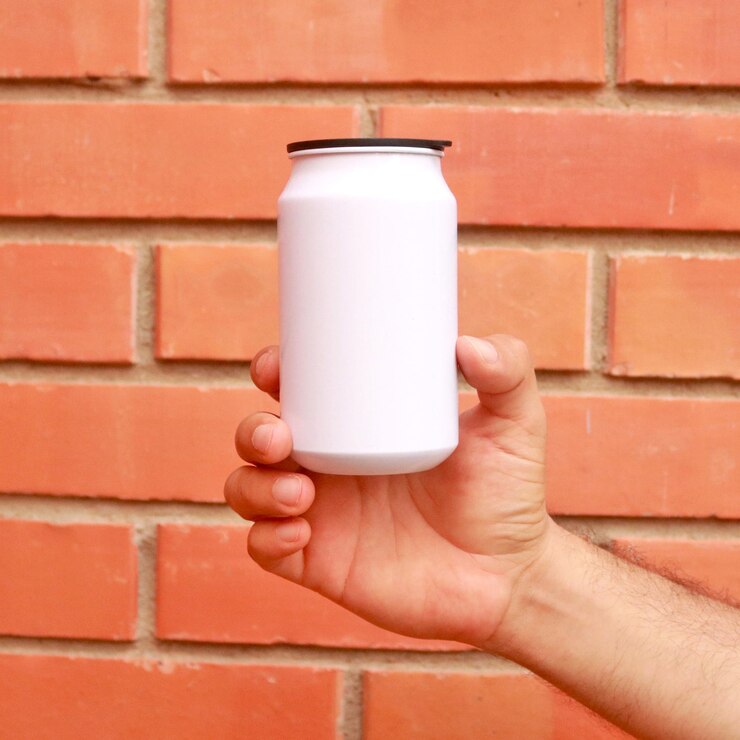 Mano d'uomo che tiene una lattina bianca su sfondo di mattoni arancioni. La bibita gassata può mockup