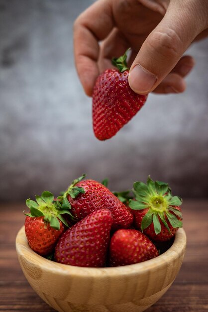 Mano d'uomo prendendo una fragola da una ciotola di legno Fragole fresche messa a fuoco selettiva verticale