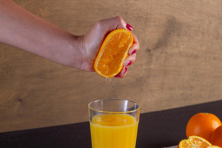 Mano de una mujer exprime el zumo de naranja en un vaso sobre una mesa, fondo de fruta de naranja