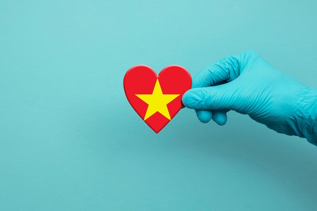 Mano degli operatori sanitari che indossa un guanto chirurgico che tiene il cuore della bandiera del vietnam