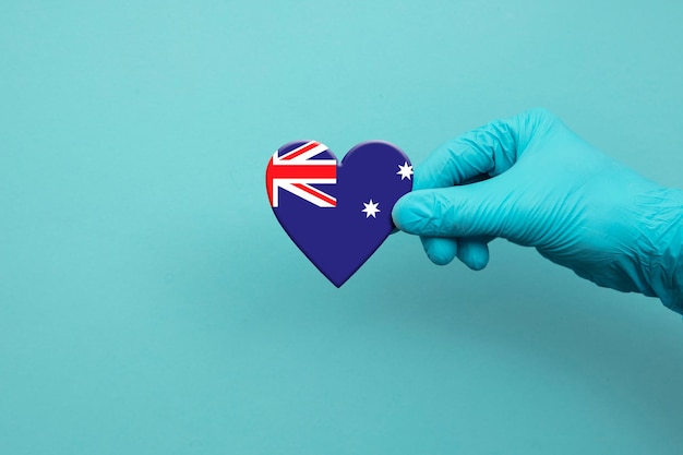 Mano degli operatori sanitari che indossa un guanto chirurgico che tiene il cuore della bandiera dell'australia