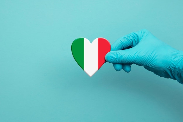 Mano degli operatori sanitari che indossa un guanto chirurgico che tiene il cuore della bandiera dell'italia