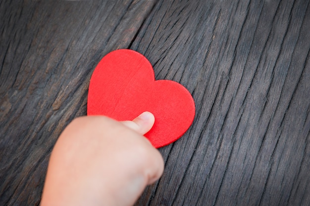 Mano dei bambini che tiene un cuore rosso su uno sfondo di legno scuro