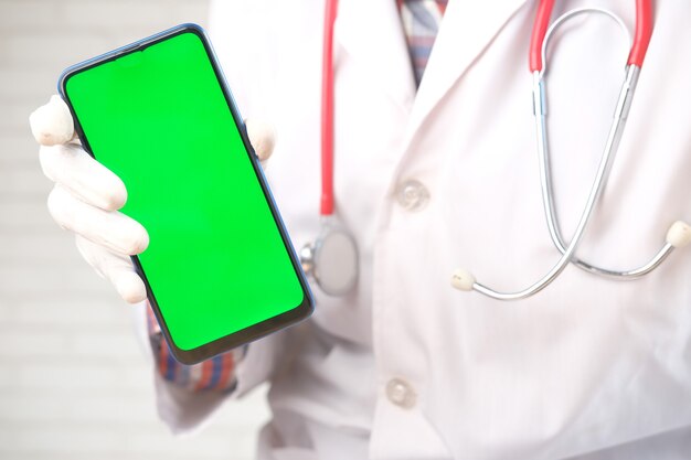 Mano dei medici in guanti protettivi che tengono telefono astuto con lo schermo verde