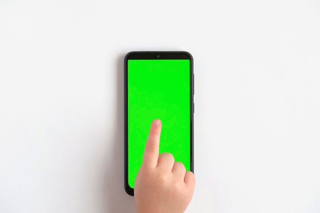 Mano del bambino che tocca facendo clic sul telefono cellulare con schermo chromakey Little Baby Finger tocca al centro del display verde del telefono vuoto Primo piano Utilizzo del dispositivo smartphone Vista dall'alto Disposizione piatta