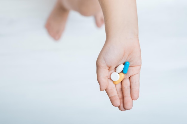Mano del bambino con pillole colorate su sfondo bianco vista dall'alto Vitamine per bambini