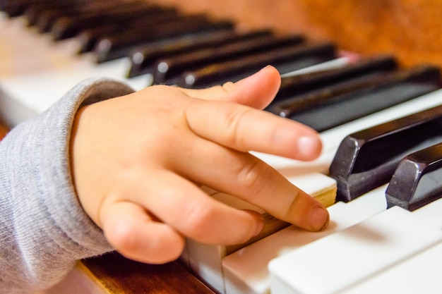 Mano del bambino sui tasti lucidi del pianoforte