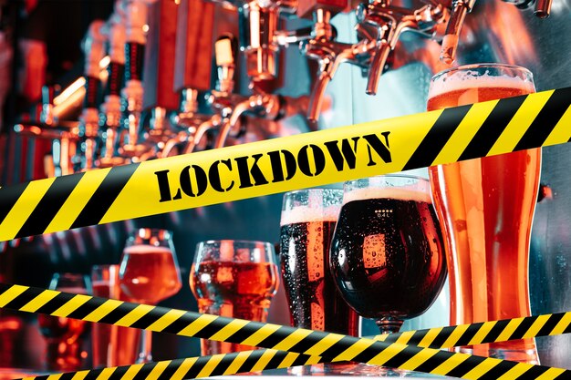 Mano del barista che versa una birra nel rubinetto con nastri di delimitazione Lockdown Coronavirus