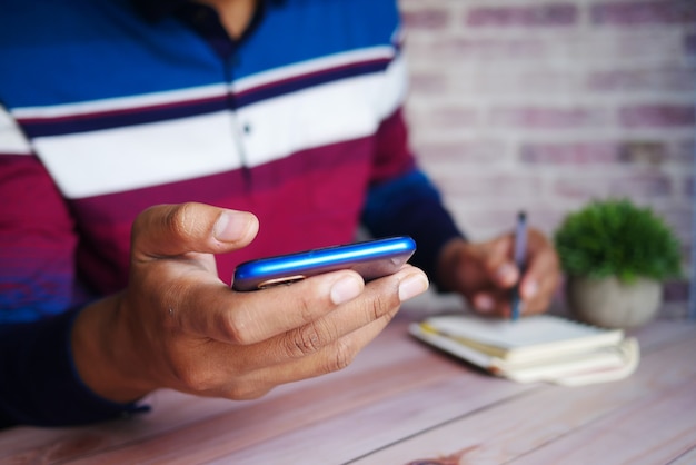 Mano del giovane che tiene lo smartphone e scrive sul blocco note mentre si trova