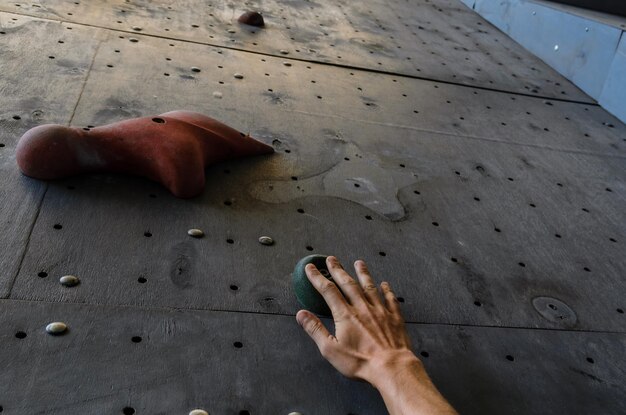 Mano del giovane su un gancio della parete artificiale di arrampicata