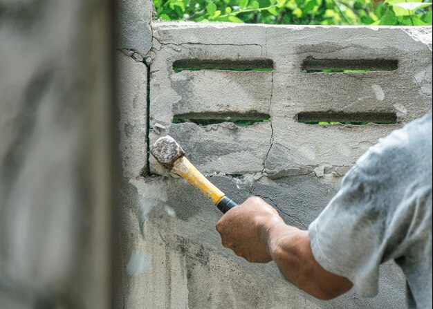 Mano del lavoratore che usa il martello che fracassa e demolisce il muro di mattoni al cantiere