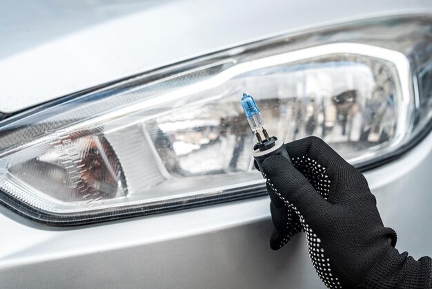 Mano del meccanico che tiene la lampadina alogena vicino al faro dell'auto, riparazione