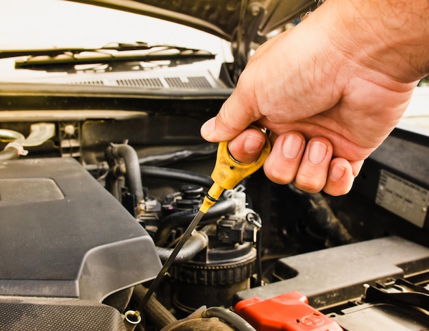 Mano del meccanico che tira su l'astina di livello dell'olio del motore dell'auto per controllare il livello dell'olio