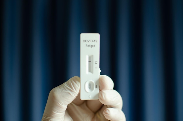 Mano del medico che mostra il test negativo Covid19 sul kit di test rapido dell'antigene per coronavirus con sfondo blu