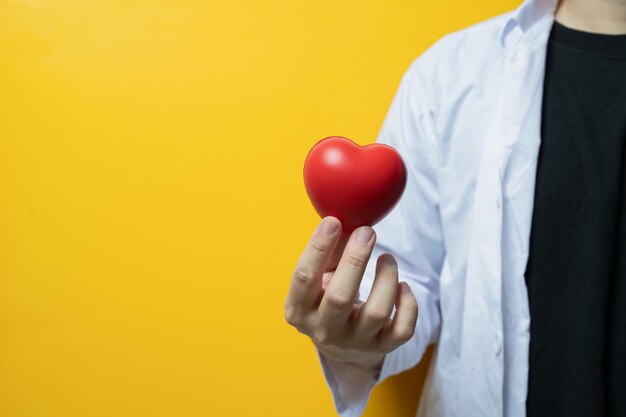 Mano del medico che tiene il cuore rosso su sfondo giallo Donazione di medicina cardiologica e concetto di assistenza sanitaria