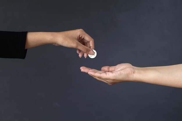 Mano del primo piano che dà moneta alla mano isolata su fondo grigio scuro. Concetto di donazione e beneficenza.