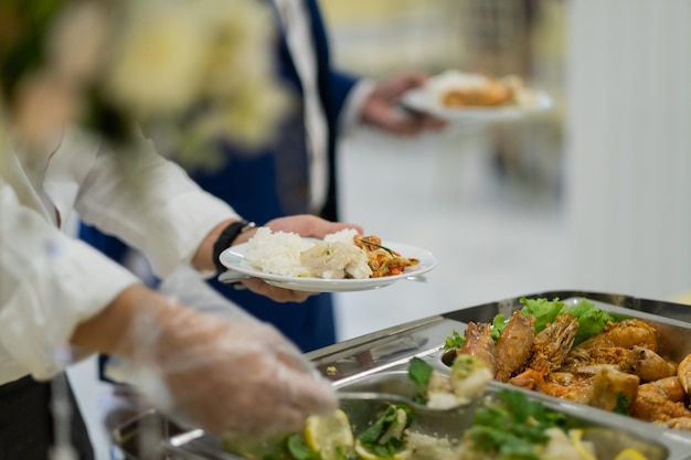 Mano del primo piano che indossa guanti che raccolgono cibo, catering, ora di cena, prevengono la malattia di Coronavirus (covid 19)