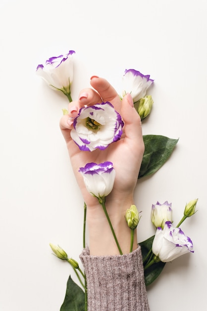 Mano delicata e fiori primaverili di eustoma sono sul tavolo bianco. Cosmetici naturali per la cura della pelle delle mani, idratanti. Cosmetici, bellezza e moda con estratti di fiori naturali