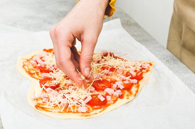 Mano dell'adolescente caucasico che versa il formaggio grattugiato sui cuori della pizza