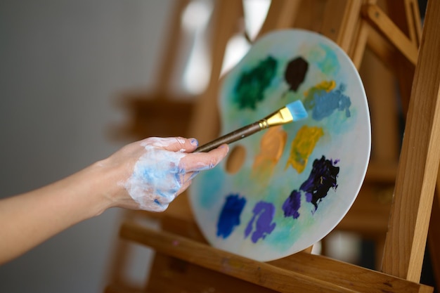 Mano dell'artista che tiene il pennello sopra la miscela di pittura ad olio sul primo piano della tavolozza di plastica