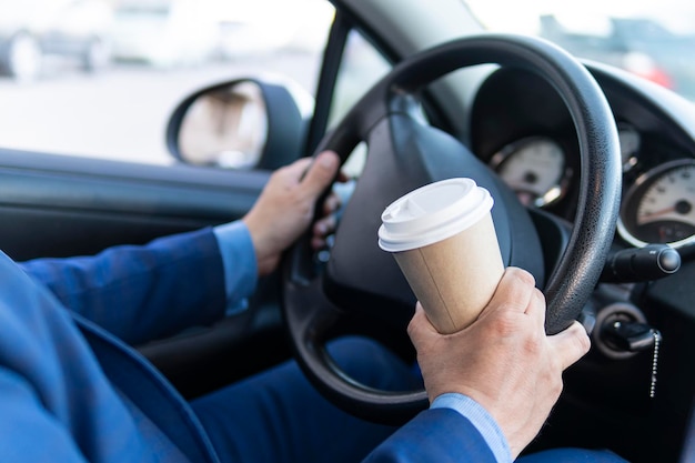 Mano dell'autista dell'uomo che tiene la tazza di caffè da portare via mentre si guida un'auto al mattino primo piano concetto di viaggio di vacanza di stile di vita della gente guida pericolosa con una tazza di caffè