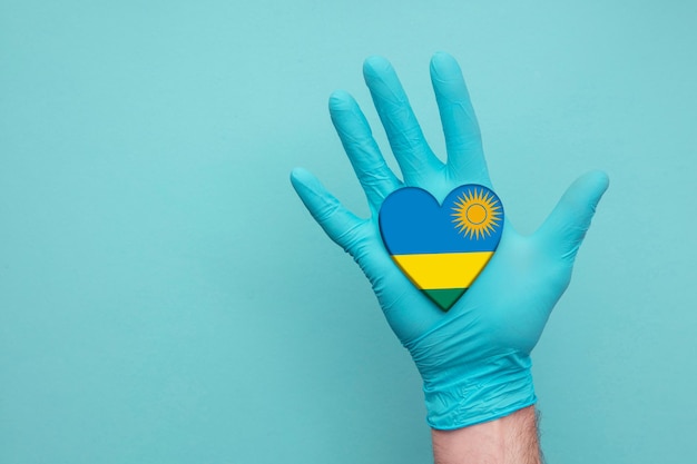 Mano dell'infermiera del cuore della salute medica del Ruanda che tiene la bandiera del cuore del paese