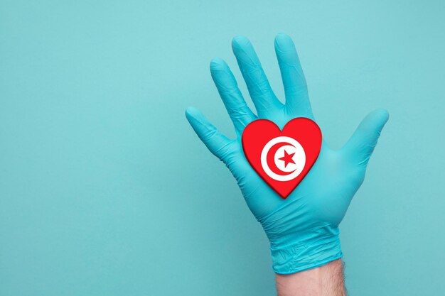 Mano dell'infermiera del cuore della salute medica della Tunisia che tiene la bandiera del cuore del paese