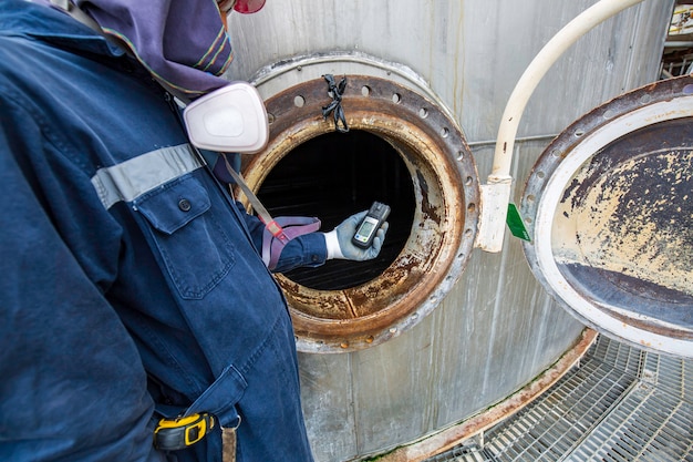 Mano dell'operaio che tiene il rilevatore di gas di ispezione di sicurezza test del gas sul serbatoio inossidabile del tombino anteriore per lavorare all'interno confinato