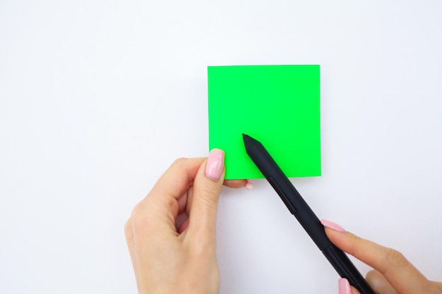 Mano dell'ufficio che tiene un adesivo di colore verde e una penna su sfondo bianco