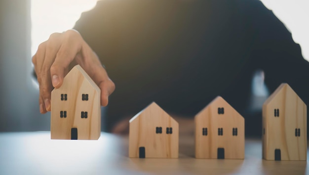 Mano dell'uomo che sceglie il modello della mini casa di legno dal modello sul tavolo di legno, pianifica l'acquisto di immobili, pianifica l'acquisto di proprietà. concetto di Scegli il meglio.