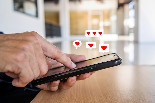 Mano dell'uomo che utilizza lo smartphone con l'icona del cuore in ufficio, guarda il messaggio degli amanti. Concetto di business tecnologico e stile di vita sociale.