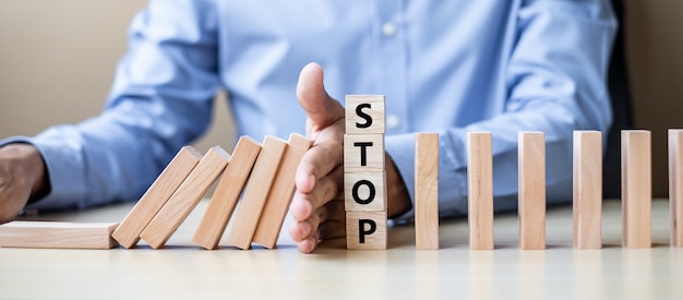 Mano dell&#39;uomo d&#39;affari che arresta i blocchi o domino di legno di caduta